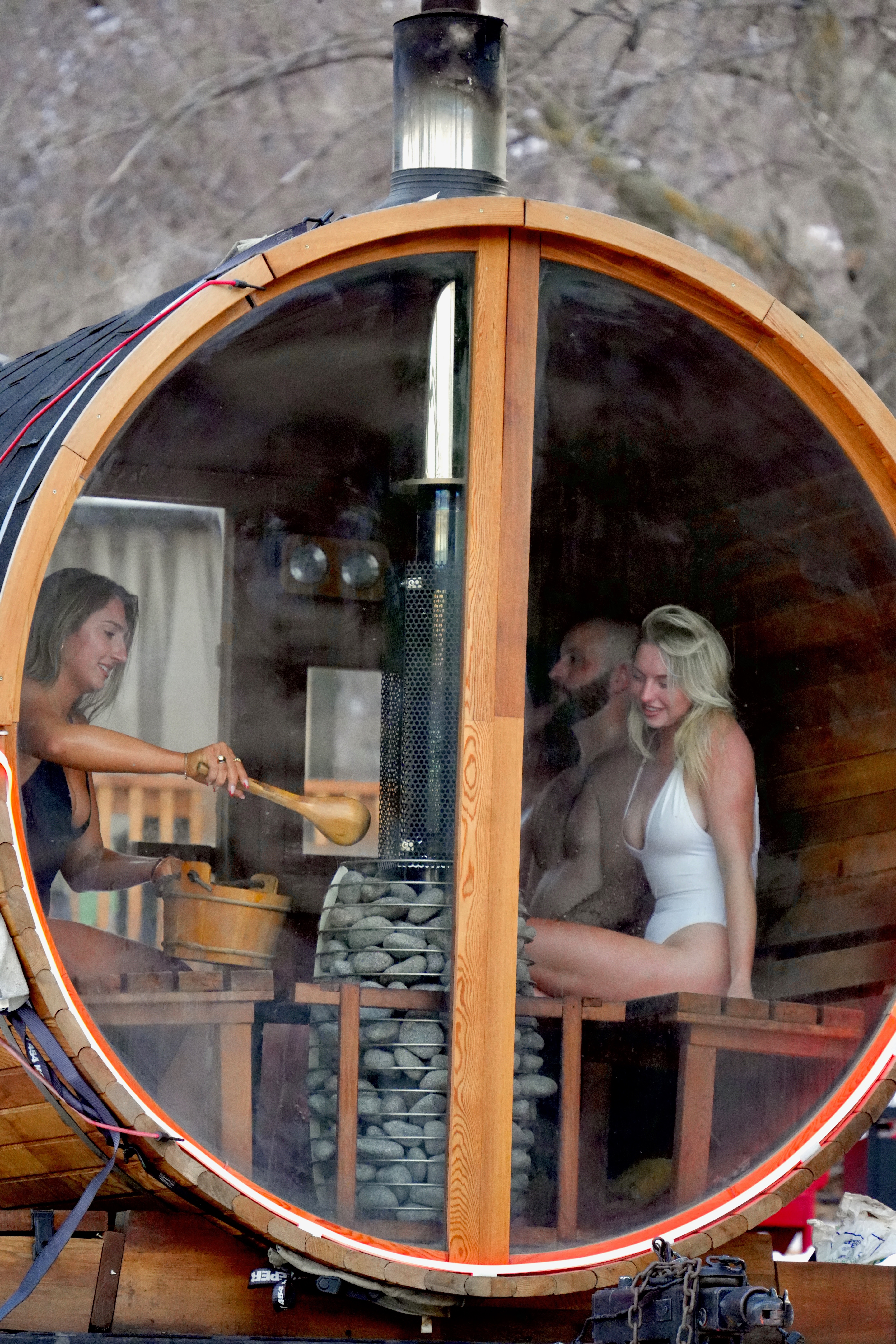 Four people inside barrel sauna with wood-fired stove, red rock view
